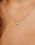 A delicate silver necklace featuring a small, round pendant with a single, sparkling diamond. The chain is fine and the pendant is set in a bezel setting. The necklace is shown against a skin tone background.