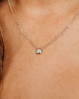 A delicate silver necklace featuring a small, round pendant with a single, sparkling diamond. The chain is fine and the pendant is set in a bezel setting. The necklace is shown against a skin tone background.