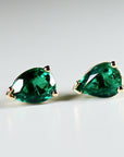 A pair of pear-shaped emerald green emerald earrings with gold settings.