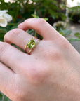 A gold peridot ring with a green oval gemstone set in the center. The ring has a simple design with two bands that wrap around the stone.