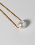 A gold chain necklace with a single large white pearl pendant.