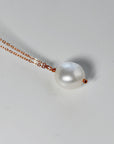 A delicate necklace featuring a large, lustrous white pearl pendant. The pearl is suspended from a fine, rose gold chain. The necklace is displayed against a plain white background, highlighting the pearl&