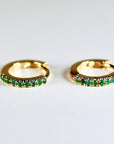 A pair of gold hoop earrings with a row of small green emerald gemstones around the edge of each hoop.