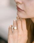A gold signet ring with a smooth, round, white top. The ring is worn on the finger of a person&