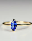 A delicate gold ring with a marquise-shaped sapphire gemstone. The sapphire is a deep blue color.