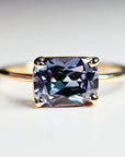 East-west emerald cut lab sapphire solitaire ring in 14k gold, displayed on a white background showing color change effect.