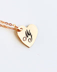 A gold heart-shaped pendant necklace with a delicate chain. The pendant has the letter "M" engraved on it.