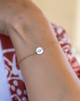 A gold chain bracelet with a small round charm featuring the letter "H" in black.