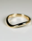 A gold band ring with a curved, wave-like design. Wavy Organic Wedding Band 14k Gold.
