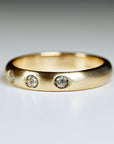 A gold band ring with three small, round, grey diamonds set into the band.