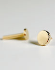 A pair of gold stud earrings with a round, flat design. The earrings are simple and minimalist.
