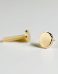 A pair of gold stud earrings with a round, flat design. The earrings are simple and minimalist.