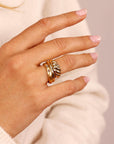A set of three gold rings stacked on a finger. The top ring is a thick, twisted band. The middle ring is a thin, plain band. The bottom ring is a thin band with three small diamonds.