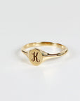 A gold signet ring with a raised oval top engraved with the letter &