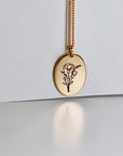 Birth Flower Necklace Gold Filled. A gold chain necklace with a round pendant featuring an engraved floral design. The pendant is oval shaped and has a delicate line drawing of a bouquet of flowers.