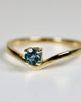 A gold ring with a V-shaped band and a single round blue sapphire gemstone.