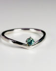 A gold ring with a v-shaped band and a single round green sapphire in the center.