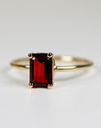 A gold ring with a red rectangular garnet gemstone. The ring is simple and elegant.