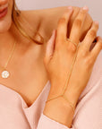 Gold chain bracelet with a delicate design. The bracelet is connected to a ring that can be worn on the finger. The bracelet is made of small gold beads and has a simple, elegant design.