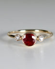 A gold ring with a large, round, red ruby gemstone and two smaller, round, white diamonds on either side.