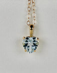 A gold chain necklace with a heart-shaped aquamarine pendant featuring a light blue gemstone.
