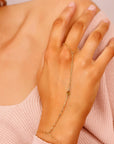 A gold chain bracelet with a teardrop-shaped charm. The bracelet is connected to a ring that can be worn on the finger. Dainty Gold Slave Bracelet, Peridot Hand Chain Bracelet