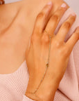 A gold chain bracelet with a teardrop-shaped charm. The bracelet is connected to a ring that can be worn on the finger. Dainty Gold Slave Bracelet, Peridot Hand Chain Bracelet