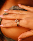 A gold ring with a clear oval-shaped gemstone set in a twisted band. The ring is worn on the middle finger of a hand.