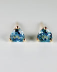 A pair of gold stud earrings with triangular blue topaz gemstones.