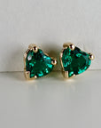 A pair of gold heart-shaped earrings with emerald green emerald gemstones.