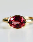 A gold ring with a large oval-shaped pink gemstone set in a bezel setting.