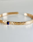 Gold hammered bangle bracelet with a blue gemstone and moon and star accents.