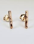 Pair of hammered gold stick stud earrings with a minimalist bar design, displayed on a white background to show texture and shape.