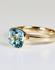 Cushion cut blue topaz solitaire ring set in 10k gold with a bezel setting, photographed on a clean white background.