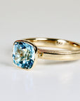 Cushion cut blue topaz solitaire ring set in 10k gold with a bezel setting, photographed on a clean white background.