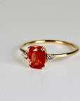 A gold ring featuring a large, rectangular orange sunstone gemstone, flanked by two smaller diamonds. The ring has a delicate band and a classic, elegant design.