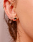 Woman wearing green sapphire bezel stud earrings in 14k gold, styled as bridal or wedding jewelry.