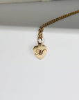Gold filled heart pendant necklace engraved with a single initial, shown on a woman’s neck. Dainty chain with a polished heart charm.