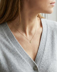 Model wearing a gold chain necklace with a small, round pendant featuring the letter "a" in script font on a hammered finish disc.