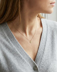 Model wearing a gold chain necklace with a small, round pendant featuring the letter "a" in script font on a hammered finish disc.