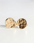 Small hammered gold disc earrings on a white background.