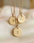 Three gold necklaces with hammered disc pendants, each featuring a different initial: S, V, and H.