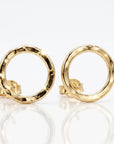 A pair of gold-colored open circle stud earrings. The earrings have a hammered texture and are displayed on a white surface. The earrings are reflective and have a post backing.