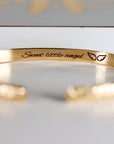 A gold cuff bracelet with "Sweet little angel" and two small wings engraved on the inside.