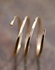 A gold-colored, three-coil spiral ring with hammered texture is shown on a blurred brown background.