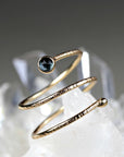 A close-up shot of a textured gold spiral ring featuring a single dark blue gemstone on a crystal background.
