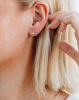 Side view of a person with blonde hair wearing a tiny gold unicorn stud earring in her earlobe.