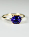 Slightly angled macro view of a gold ring holding an east-west set oval purple faceted gemstone on a white background.