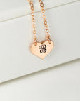 A rose gold necklace with a heart pendant engraved with the letter S rests against a white background.