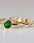 Two gold rings are stacked, with a plain gold band on the bottom and a gold twisted rope ring on top, both in soft focus.